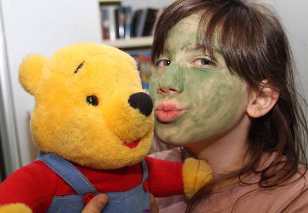 Ein Mädchen mit einer Gesichtsmaske umarmt einen Winnie Puh Bären.