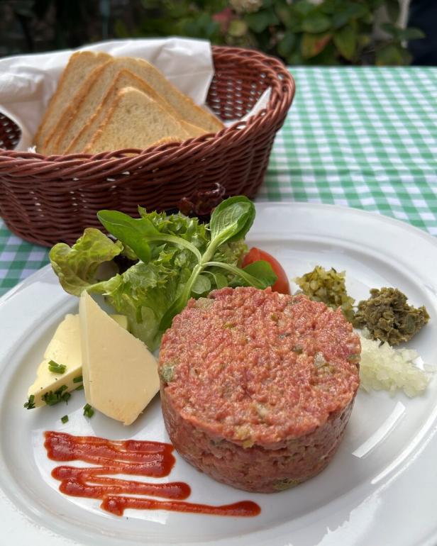 Beef Tatar am Teller, die Zutaten sind rund um das Fleisch angeordnet. Gemischt wird selbst.