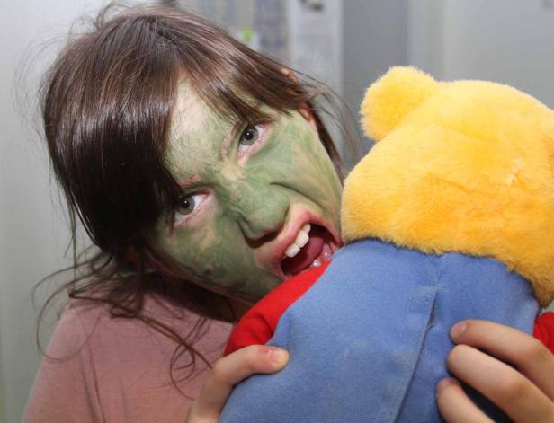 Ein Mädchen mit grüner Gesichtsmaske beißt in einen Teddybären.