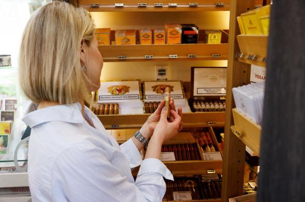 Eine Frau befindet sich in einer Trafik und hält eine Zigarre in der Hand.