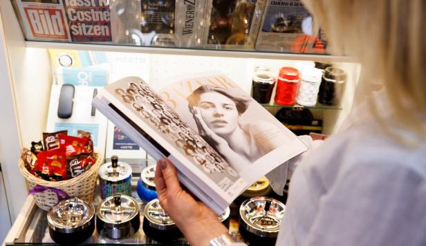 Eine Frau blättert in einer Zeitschrift in einer Trafik.
