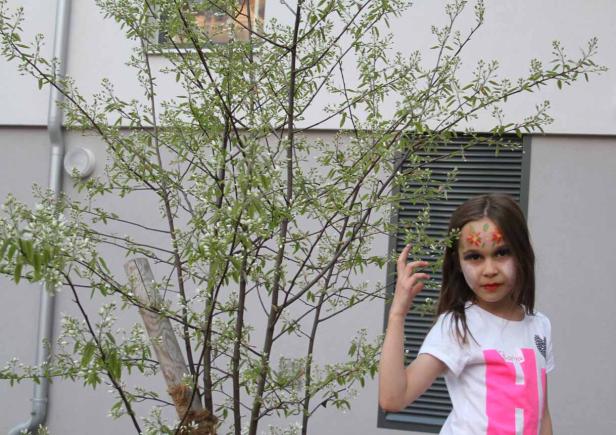 Ein Mädchen mit Blumenmalerei im Gesicht steht neben einem blühenden Baum.