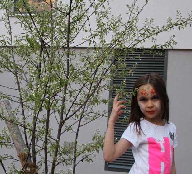 Ein Mädchen mit Gesichtsbemalung steht neben einem blühenden Baum.