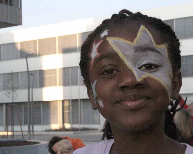 Ein junges Mädchen mit einer aufgemalten Sternenmaske im Gesicht lächelt.