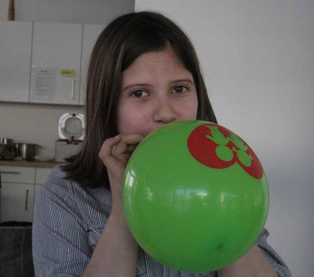Ein Mädchen pustet einen grünen Ballon auf.