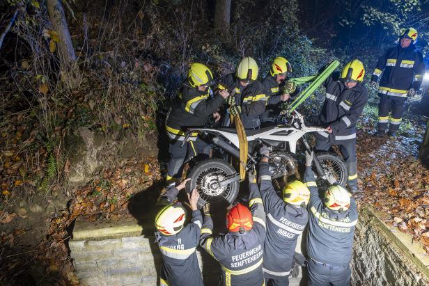 Mehrere Feuerwehrmenschen ziehen ein Motorrad aus einem Graben.