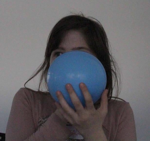 Ein Mädchen hält einen blauen Ballon vor ihr Gesicht.