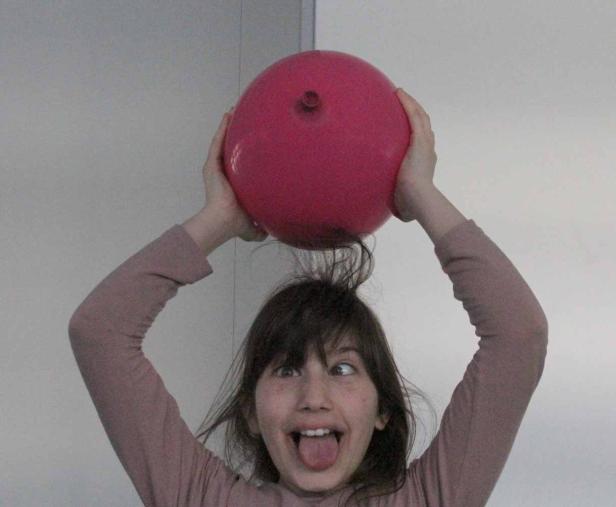 Ein Mädchen hält einen roten Ballon über den Kopf und macht ein albernes Gesicht.