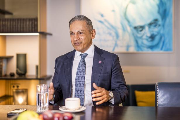 Sherrif Karamat sitzt in einem blauen Anzug am Tisch, vor ihm ein Kaffee.