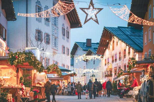 Blick ins historische Zentrum. Alte Häuser, Menschen gehen in der Innenstadt, Weihnachtsstände stehen da, Weihnachtsbeleuchtung hängt.