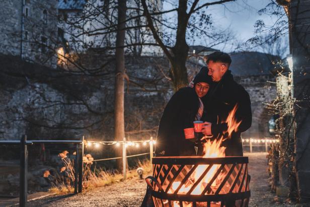 Eine Frau kuschelt sich vor einem Lagerfeuer an einen Mann. 