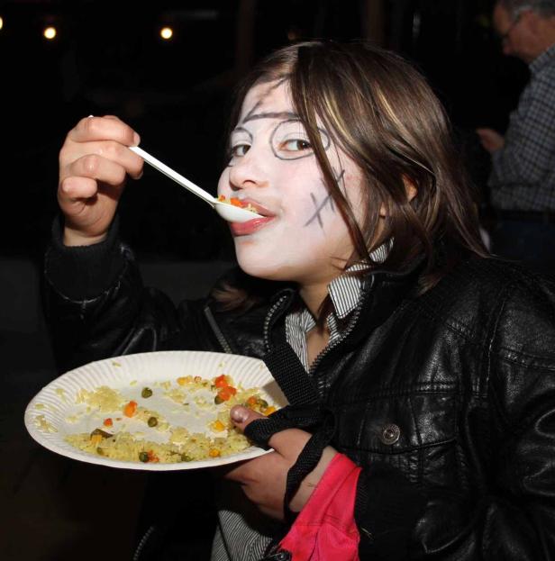 Ein Mädchen mit Gesichtsbemalung isst Reis mit Gemüse von einem Pappteller.