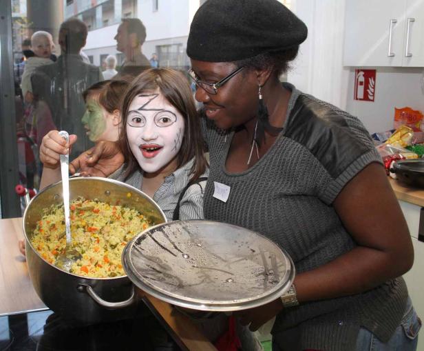 Ein Mädchen mit Gesichtsbemalung hält einen Topf mit Reis, während eine Frau daneben steht.