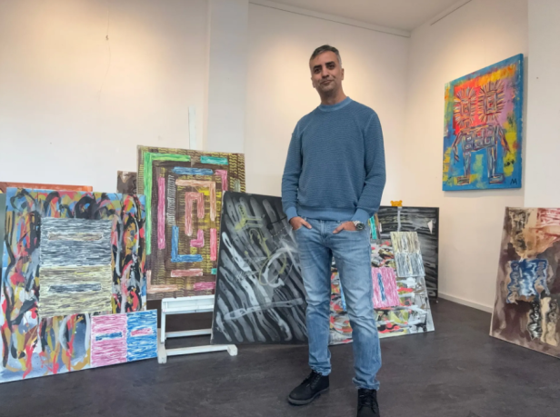 Galerist Kerem Akar steht vor Gemälden