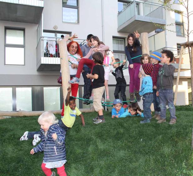 Eine Gruppe Kinder spielt auf einem Spielplatz vor einem Wohnhaus.