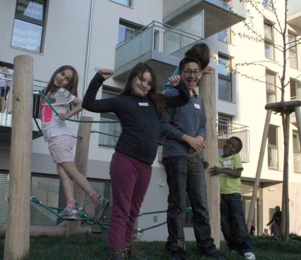 Eine Gruppe Kinder spielt auf einem Spielplatz vor einem Wohnhaus.