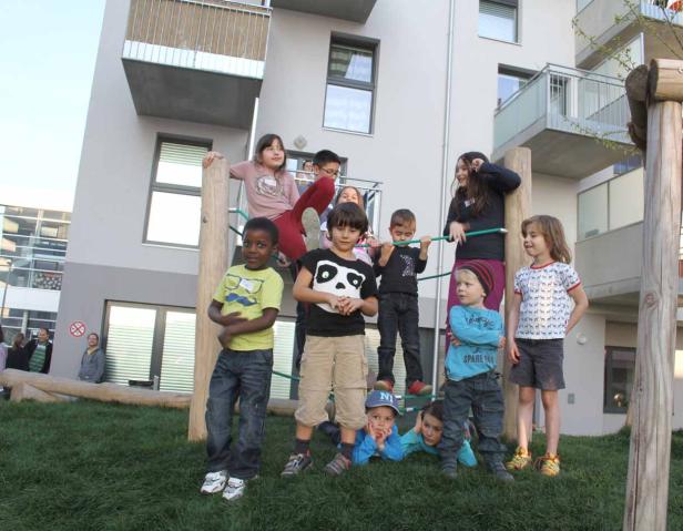 Eine Gruppe Kinder spielt auf einem Spielplatz vor einem modernen Wohngebäude.