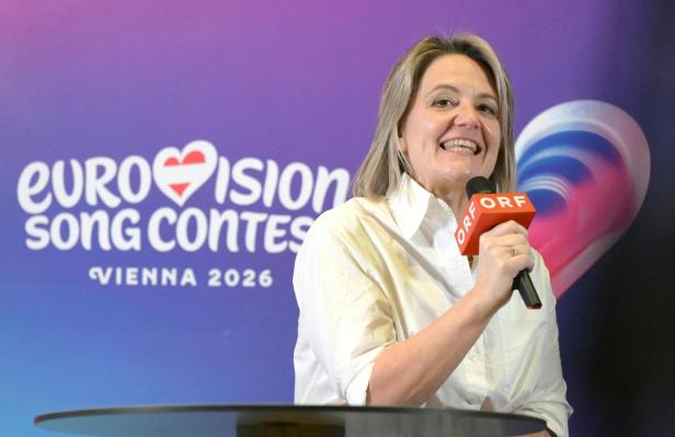 Eine Frau spricht mit einem ORF-Mikrofon vor einem Eurovision Song Contest 2026 Wien Hintergrund.