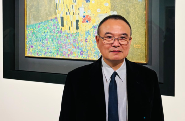 Mann mit Brille steht vor Gustav Klimts Gemälde „Der Kuss“ in einem Museum.