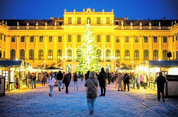 Auf dem Weihnachtsmarkt vor Schloss Schönbrunn flanieren abends viele Menschen.