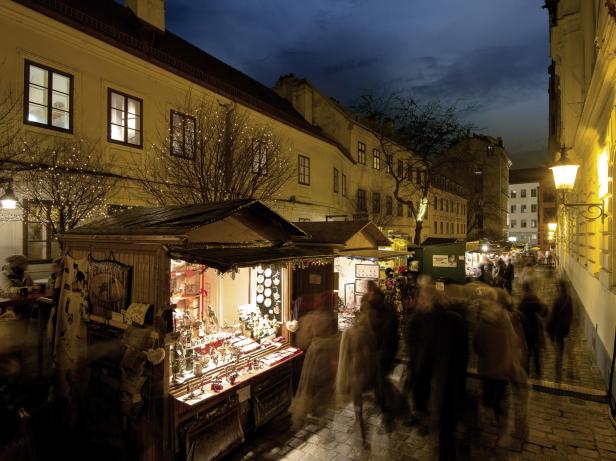 Ein belebter Weihnachtsmarkt erstreckt sich in einer Gasse des Wiener Spittelbergs zwischen beleuchteten Gebäuden.