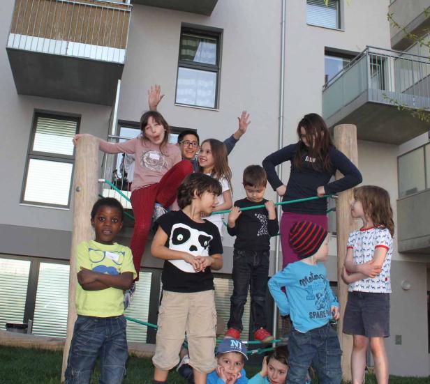Eine Gruppe von Kindern spielt auf einem Spielplatz vor einem Wohnhaus.