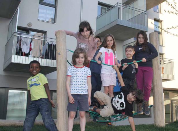 Eine Gruppe Kinder spielt auf einem Spielplatz vor einem Wohnhaus.