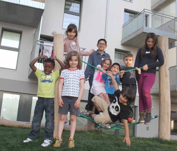 Eine Gruppe Kinder spielt auf einem Klettergerüst vor einem Wohnhaus.