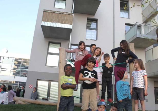 Eine Gruppe Kinder spielt auf einem Klettergerüst vor einem modernen Gebäude.