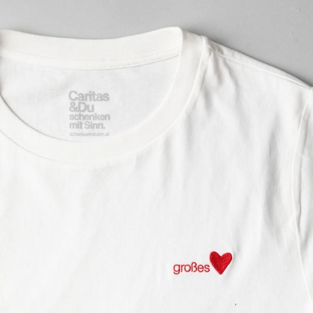 Weißes T-Shirt mit rotem Schriftzug 'großes' und rotem Herz auf der Brust, innen Aufdruck 'Caritas & Du schenken mit Sinn.'