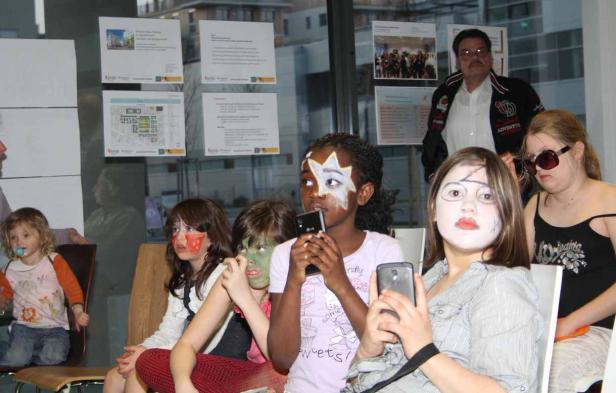 Eine Gruppe von Kindern mit Gesichtsbemalung sitzt in einem Raum und hält Smartphones in den Händen.