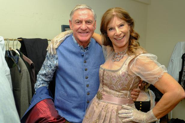 Ein lächelndes Paar in Tracht posiert, die Frau im Dirndl, der Mann mit Weste und Handschuhen.