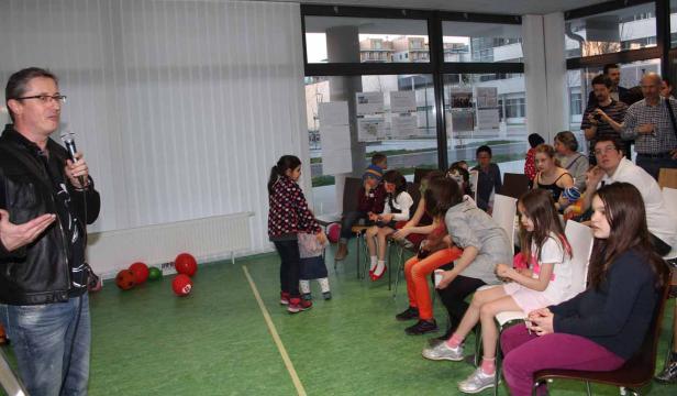 Ein Mann spricht mit einem Mikrofon vor einer Gruppe von Kindern und Erwachsenen.