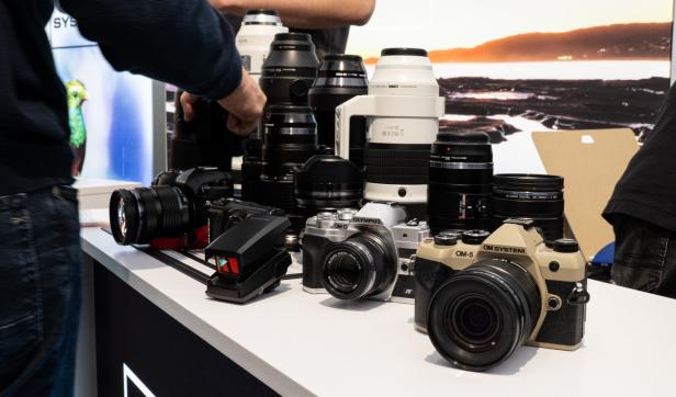 Mehrere Kameras und Zubehör, wie Objektive liegen auf einem Tisch. Eine männliche Hand hantiert mit einer Kamera.
