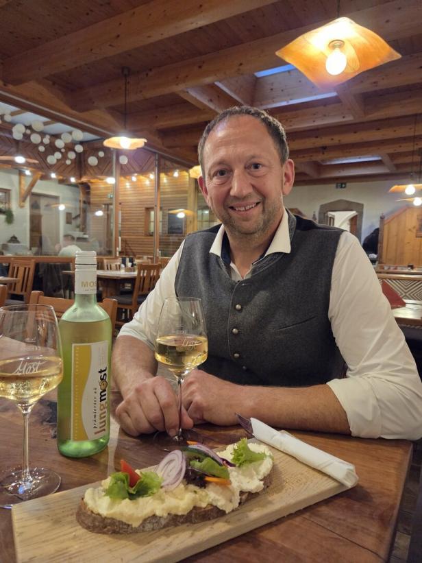 Mann sitzt vor einem Jausenbrett mit einem Käsebrot