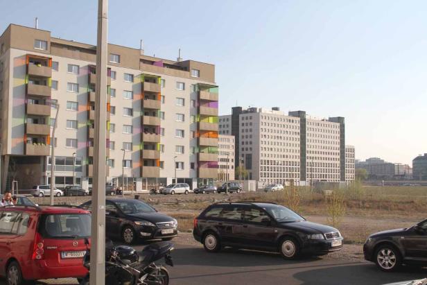 Mehrere Autos stehen vor einem Wohnhaus mit farbigen Balkonen.