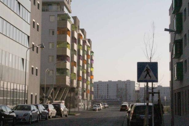 Eine Straße in einer Stadt mit modernen Wohnhäusern und einem Fußgängerüberweg.