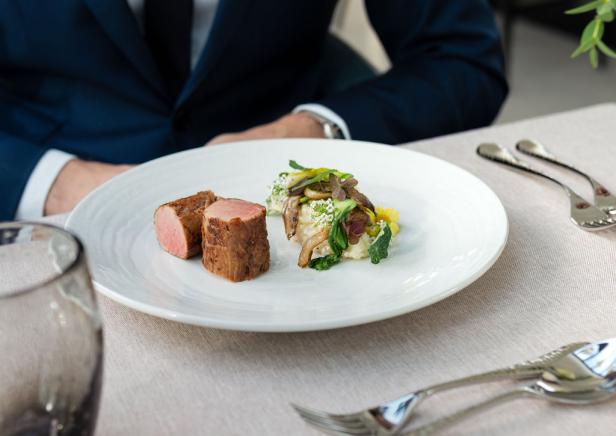 Ein Mann isst ein Stück Fleisch, das schön auf einem Teller angerichtet ist 