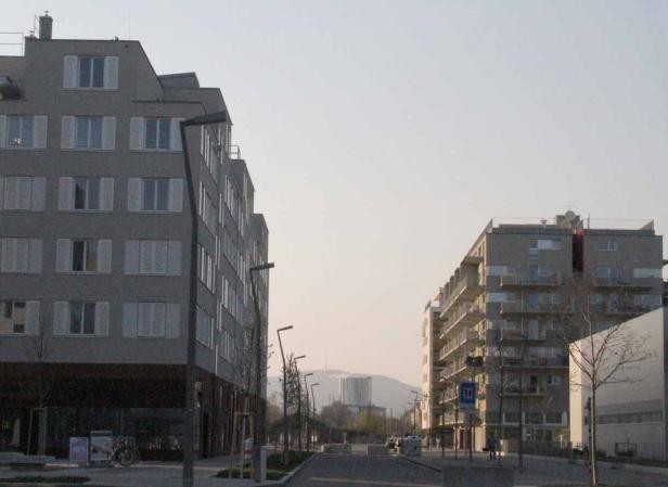 Blick auf eine Straße zwischen zwei Wohngebäuden mit einem Turm im Hintergrund.