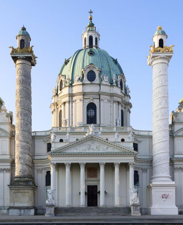 Barockkirche mit großer Kuppel, verzierten Säulen und Statuen an der Fassade bei klarem Himmel.