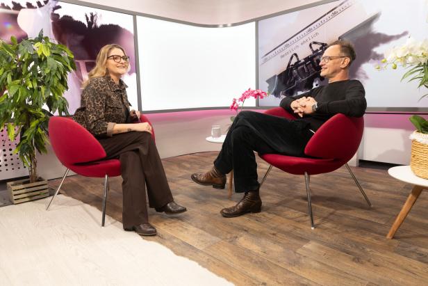Zwei Personen sitzen sich in roten Sesseln gegenüber und unterhalten sich in einem modern eingerichteten Raum mit Pflanzen.