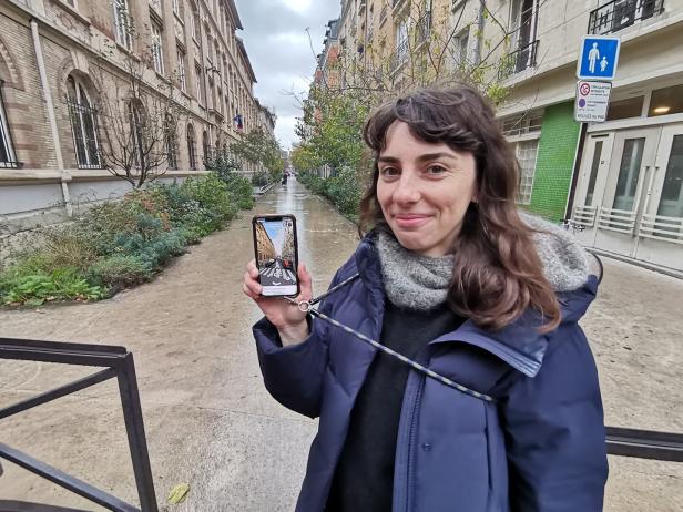 Eine Frau zeigt auf einem Handy, wie die Straße, in der sie steht, früher ausgesehen hat.