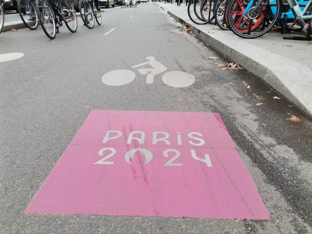Radfahrer-Piktogramm und ein pinkes Paris 2024 Piktogramm auf einer Straße.