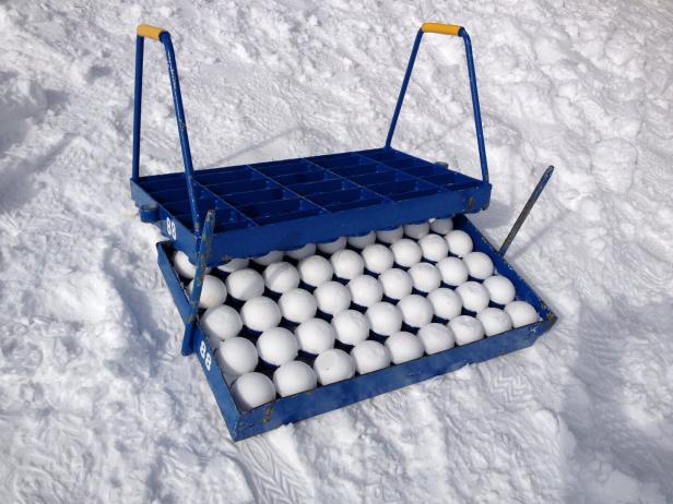 Blauer Eierkarton mit mehreren weißen Eiern, auf Schnee liegend, mit geöffnetem Deckel und zwei Griffen.