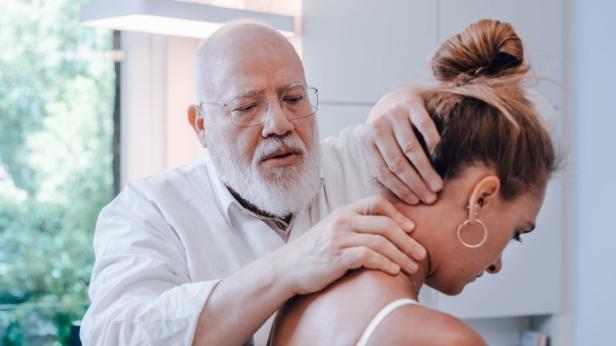 Ein Mann mit Bart und weißem Hemd massiert den Nacken einer Frau.