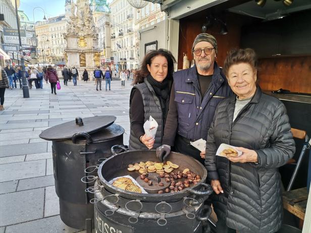Zwei Frauen und ein Mann bei einem Maronistand am Graben.