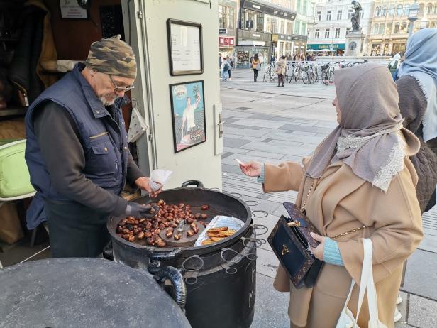 Eine Frau mit Kopftuch kauft bei einem Mann mit Haube Maroni.