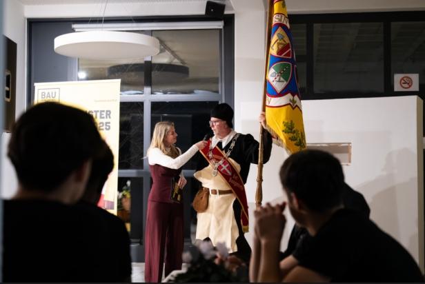 Eine Frau hält einem Mann in einem Kostüm ein Mikrofon zum Mund.