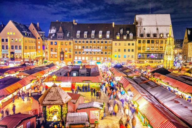 Viele Menschen schlendern zwischen festlich beleuchteten Buden auf einem Weihnachtsmarkt vor historischen Gebäuden.