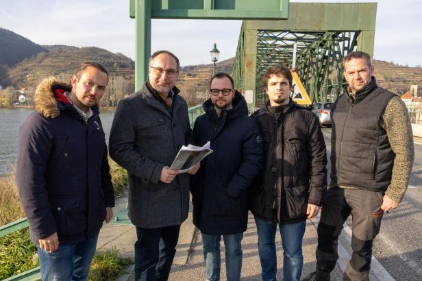 Mehrere Männer in Winterjacken stehen vor der Donaubrücke, die Krems mit Mautern verbindet.